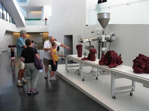 Roxy Paine, Visitors viewing "Scumak No. 2" at The Nelson-Atkins Museum of Art, Kansas City, Missouri, 2011. Aluminum, computer, conveyor, electronics, extruder, stainless steel, polyethylene, Teflon, 90 × 276 × 73 ̋. Photography by Adrianne Russell.